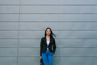 Self confident Asian female entrepreneur standing on the street near urban building and looking at camera - ADSF20729