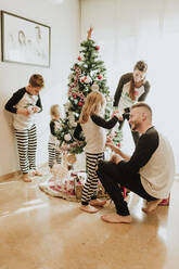 Glückliche Familie beim gemeinsamen Schmücken des Weihnachtsbaums zu Hause - GMLF00947