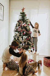 Bruder und Schwestern schmücken den Weihnachtsbaum zu Hause - GMLF00950