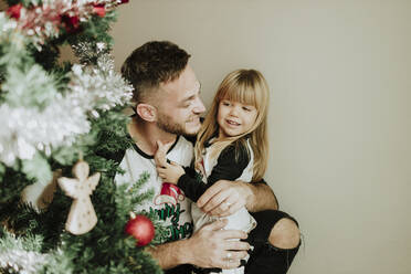 Smiling father embracing daughter by Christmas Tree at home - GMLF00954