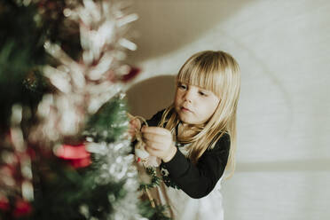 Blondes Mädchen schmückt Weihnachtsbaum an der Wand zu Hause - GMLF00958