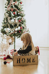 Verspieltes Mädchen sitzt in einer Schachtel am Weihnachtsbaum zu Hause - GMLF00966