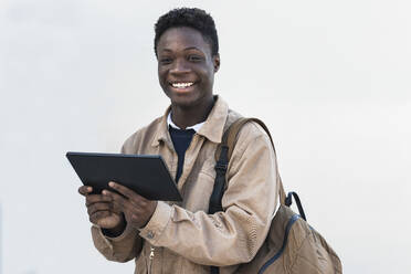 Lächelnder afrikanischer Mann mit digitalem Tablet vor weißer Wand - PNAF00612