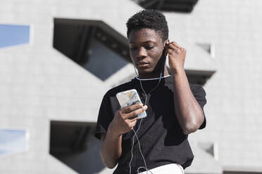 Junger Mann benutzt sein Smartphone, während er an einem sonnigen Tag Musik hört - PNAF00614