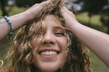 Smiling blond woman with hand in hair at park - DSIF00321