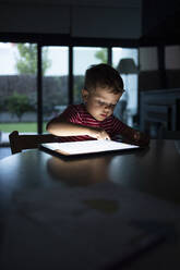 Boy using digital tablet while sitting at table in home - IFRF00378