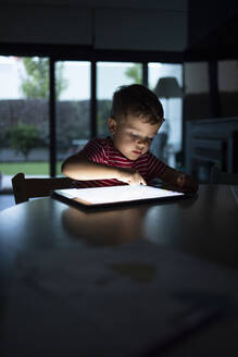 Junge benutzt digitales Tablet, während er zu Hause am Tisch sitzt - IFRF00378