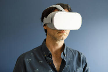 Man watching movie through virtual reality simulator against blue wall - IFRF00401