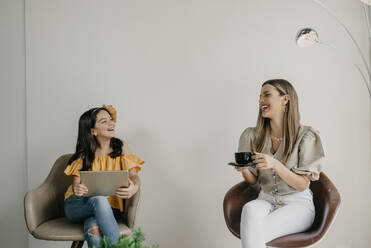 Mother and daughter smiling at each other while sitting in waiting room - DSIF00327