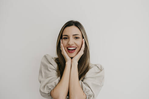 Surprised woman with hand on chin smiling against white background - DSIF00334