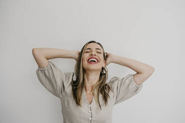 Laughing woman with hands behind head against white background - DSIF00337