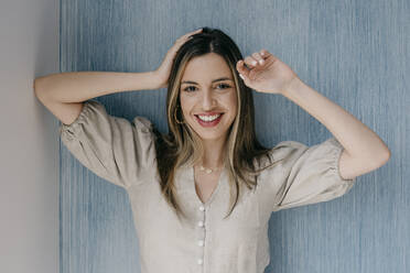 Lächelnde Frau mit Kopf in der Hand an die Wand gelehnt - DSIF00338