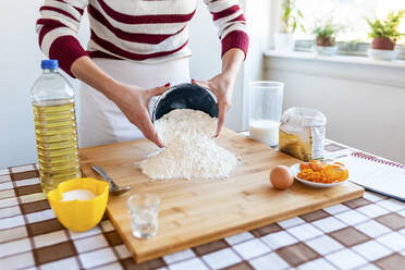 Frau gießt Mehl auf Schneidebrett in Küche zu Hause - WPEF03986