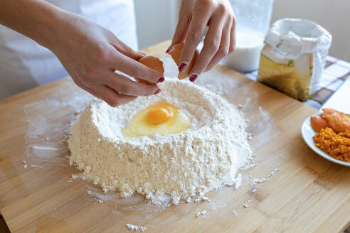 Frau schlägt Ei in Mehl auf einem Schneidebrett in der Küche auf - WPEF03991