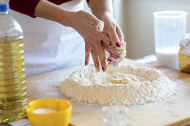 Frau reinigt ihre Hände beim Mischen von Eiern und Mehl auf einem Schneidebrett in der Küche - WPEF03993