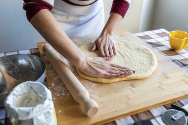 Frau, die den Teig mit den Händen auf dem Schneidebrett plattdrückt, um Croissants in der Küche herzustellen - WPEF04005