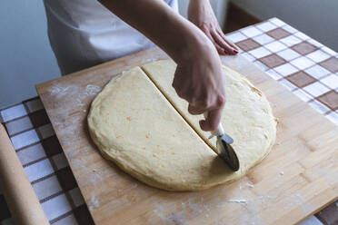 Frau schneidet Teig mit Pizzaschneider, um Croissants in der Küche zu machen - WPEF04017