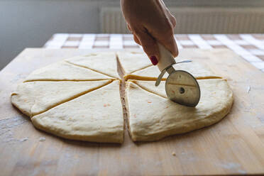 Frau schneidet Teig mit einem Pizzaschneider in Scheiben, um Croissants herzustellen - WPEF04018