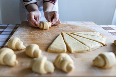 Frau macht Croissants aus geschnittenem Teig auf einem Schneidebrett in der Küche - WPEF04019