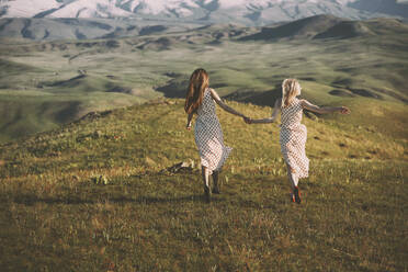 Playful female friends running while holding hands against hills - AZF00182