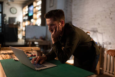 Gelangweilter Handwerker, der im Atelier am Laptop sitzt - CAVF92666