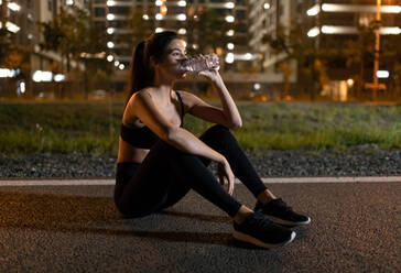 Sportlerin trinkt nachts auf der Strecke Wasser - CAVF92672