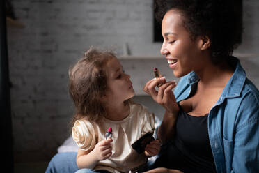 Mother teaching daughter to apply lipstick - CAVF92685