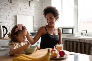 Ethnic mother stroking daughter during breakfast - CAVF92692