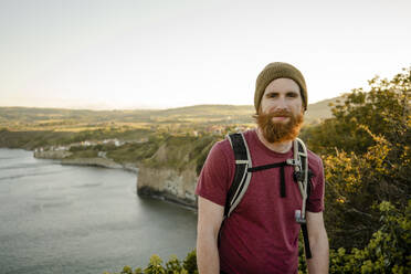 Smiling Bearded man with view of Robins Hood's Bay behind at sun - CAVF92750