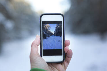 Deutschland, Brandenburg, Menschliche Hand hält Smartphone in Winterlandschaft - ASCF01562