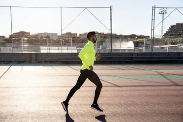 Male athlete jogging on running track at sports court during sunny day - AMPF00006