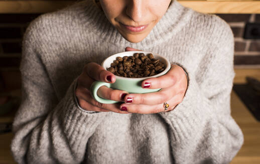 Junge Frau riecht an frischen Kaffeebohnen in einer Tasse im Café - DAMF00717