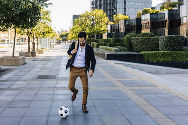 Businessman playing with soccer ball while running on footpath - XLGF01143