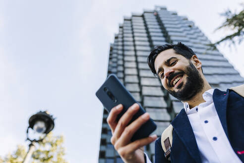 Lächelnder Geschäftsmann, der ein Smartphone benutzt, während er in der Stadt steht - XLGF01146