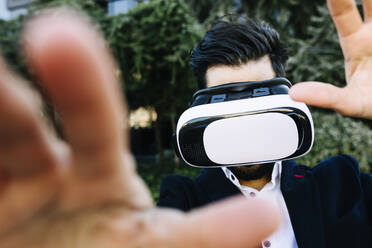 Geschäftsmann mit Virtual-Reality-Headset, der im Freien stehend seine Hand ausstreckt - XLGF01153