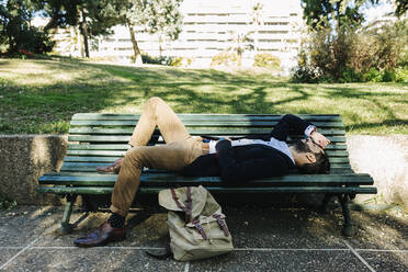 Businessman resting while lying on bench at park - XLGF01158