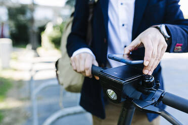 Businessman renting bicycle through mobile phone while standing at bicycle station - XLGF01164