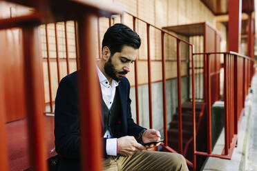 Businessman using mobile phone while sitting on steps - XLGF01171