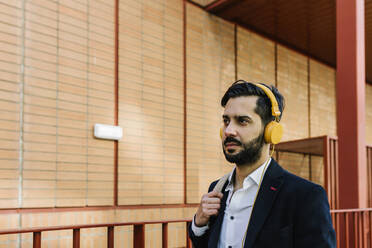 Businessman wearing headphones looking away while standing outdoors - XLGF01178