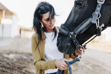 Woman checking horse bridle while standing outdoors - MRRF00869