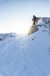 Male skier standing on snowy mountain peak against sky during sunrise - JAQF00277