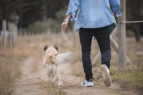 Mann geht mit Hund auf unbefestigtem Weg spazieren - SNF01161