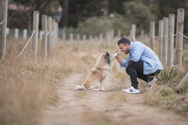 Mid adult man playing with dog while crouching on dirt road - SNF01162