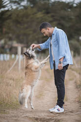 Man feeding dog while standing on dirt road - SNF01166