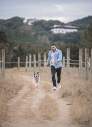 Playful man running with dog on dirt road - SNF01170