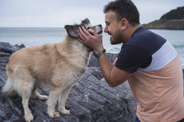 Happy man embracing dog standing on rock formation at beach - SNF01177