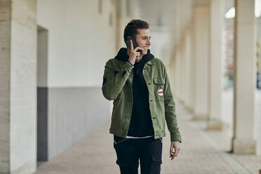 Lächelnder junger Mann, der mit seinem Handy telefoniert und in eine Spielhalle schaut - ACPF01104