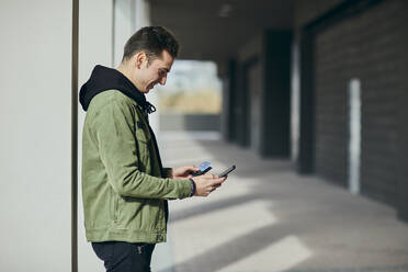 Man with credit card doing online shopping through mobile phone while standing in arcade - ACPF01112