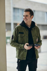 Lächelnder gut aussehender Mann mit Mobiltelefon, der eine Kreditkarte hält und wegschaut - ACPF01113
