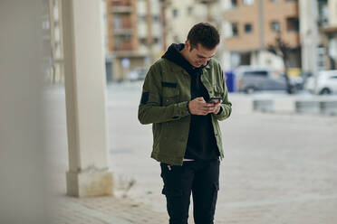 Junger Mann, der ein Mobiltelefon benutzt, während er in einer Spielhalle steht - ACPF01118